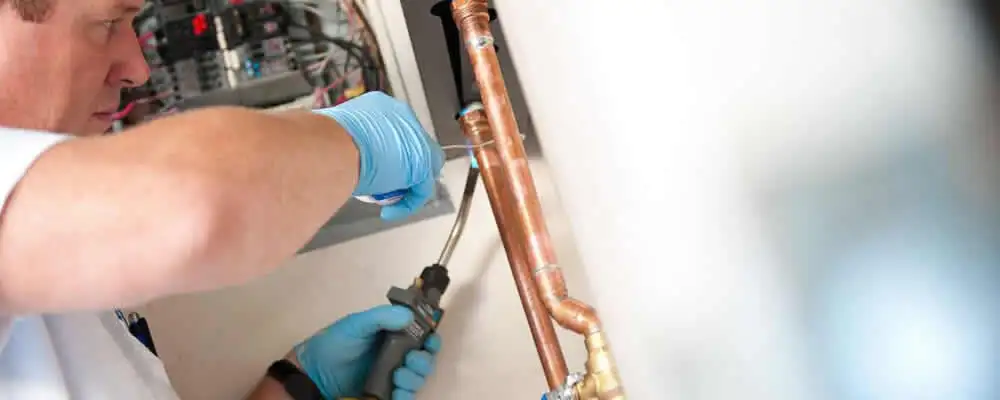 Water heater repair technician testing copper pipe connections and controls in Los Angeles, CA